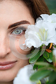 Young girl with green eyes admires blooming azaleas in a botanical garden. Closeup of butiful girl with flowers