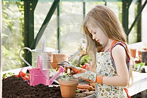 Young girl in greenhouse putting plant in pot