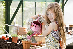 Young girl in greenhouse watering potted plant