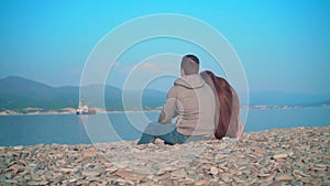 Young girl with a guy sitting on the beach. The girl lays her head on the guy`s shoulder.