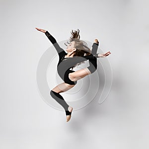 Young girl gymnast in black sport body and uppers jumping and making dymnastic pose in air over white background