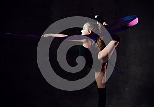 Young girl gymnast in black sport body and uppers standing sideways and making exercise with blue gymnastic tape