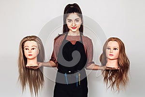 Young girl hairdresser holds in hands two mannequin heads.