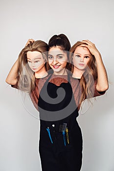 Young girl hairdresser holds in hands two mannequin heads. Woman with three heads.