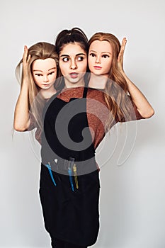 Young girl hairdresser holds in hands two mannequin heads. Woman with three heads.