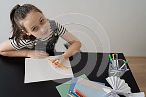 Young girl hand making craft using paper, scissors and pencils