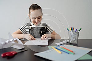 Young girl hand making craft using paper, scissors and pencils