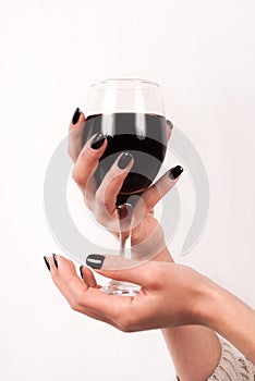 Young girl hands with black nails holding glass with red wine, close up