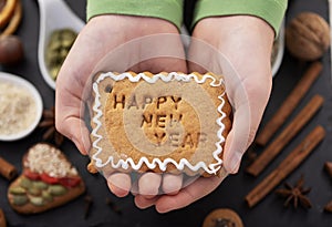 Young girl hands hold gingerbread biscuit with happy new year text and white icing