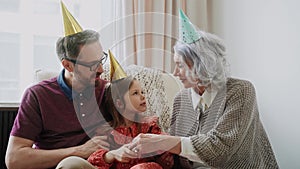 Young girl has fun and cuddles with her father and grandmother at birthday party