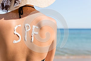 Young girl has spf word on her back made of sun cream at the beach. Sun protection factor concept