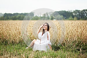 A young girl in a hat is a boatman enjoying the nature of a wheat field. Beautiful girl in white dress runs on the field at sunset