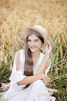 A young girl in a hat is a boatman enjoying the nature of a wheat field. Beautiful girl in white dress runs on the field at sunset