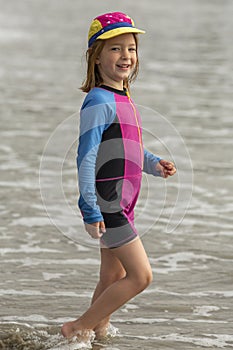 Young girl in a hat and colorful swimming suit having fun splashing at the beach
