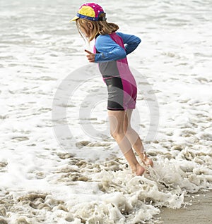 Young girl in a hat and colorful swimming suit having fun splashing at the beach