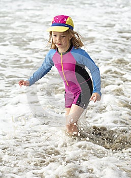 Young girl in a hat and colorful swimming suit having fun splashing at the beach