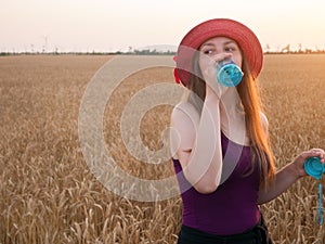 Young girl in hat holds a bottle of water in hand and drinks water in wheat field.Weight loss active lifestyle body care