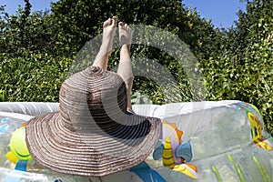 Young girl  in hat and swimsuit lying in the inflatable swimming pool. Vacation 2020