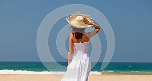 Young girl in hat and white dress looking at sea coast