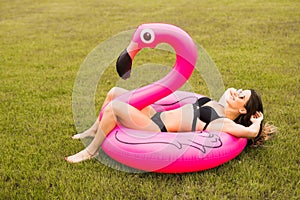 Young and girl having fun and laughing and having fun on the grass near the pool on an inflatable pink flamingo in a bathing