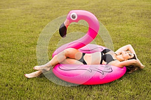 Young and girl having fun and laughing and having fun on the grass near the pool on an inflatable pink flamingo in a bathing