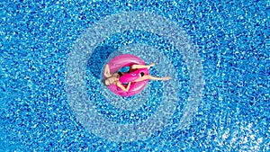 Young girl having fun and laughing and having fun in the pool on an inflatable pink flamingo in a bathing suit in summer from abov