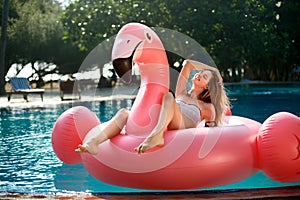 Young and girl having fun and laughing on an inflatable giant pink flamingo pool float mattress in a bikini