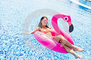 Young girl having fun and laughing on an inflatable giant pink flamingo pool float mattress in a bikini. Attractive tanned woman l