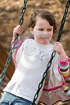 Young girl having fun outside at park on a playground swing set