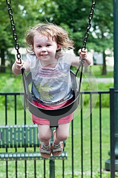 Young girl having fun outside at park on a playground swing set