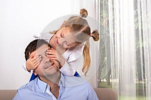 A young girl  is having fun playing with her dad, closing his eyes so that he can guess who it is