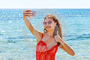 Young girl having fun taking smartphone selfie pictures of herself. travel holidays. happy young woman giving hand sign thumbs up