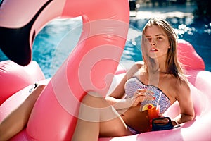 Young and girl having lies in the sun an inflatable giant pink flamingo pool float mattress with a cocktail glass