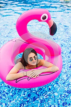 Young and girl having lies in the sun an inflatable giant pink flamingo pool float mattress with a cocktail glass. Attractive