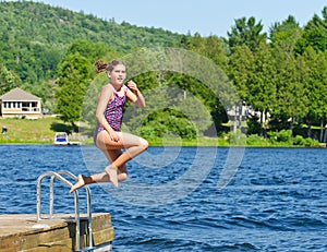 Young girl having summer fun jumping into lake of the dock