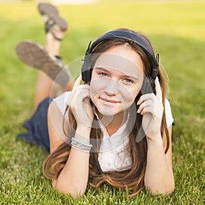 Young girl in headphones enjoys the music lying on the green grass. Pleasure.