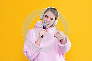 young girl in headphones with microphone on yellow background. point finger with selective focus