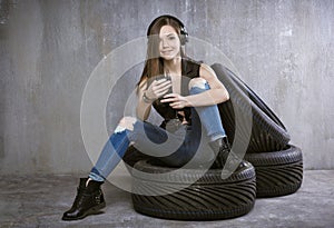 young girl with headphones and mobile phone, sitting on car tires on a background of gray concrete wall