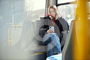 Young girl with headphones sitting in modern tram and looking on mobile phone, listening to music in headphones. Blurred