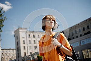 Young girl with headphones in a yellow t-shirt and with a backpack walks along a city street on a summer sunny day