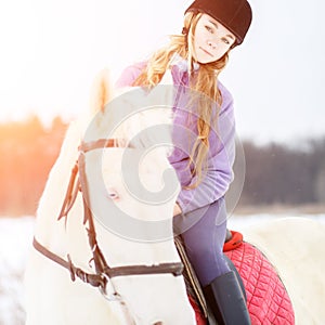 Young girl in helmet riding white horse on field