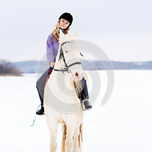 Young girl in helmet riding white horse on field