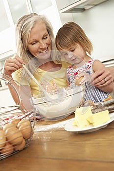 Young Girl Helping Grandmother To Bake Cakes In Kitchen