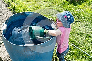 Young girl helping in the vegetable garden and fills a large watering can in a blue barrel