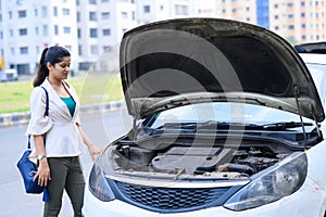 Young girl and her broken car with open hood.