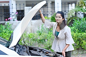 Young girl and her broken car with open hood.