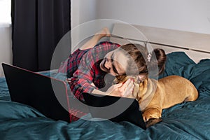 Young girl and her dog french bulldog working in bed at a laptop during quarantine