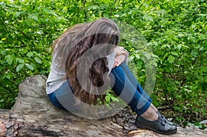 A young girl with her long hair sits in the park with her face covered. The girl is somewhat upset, upset.Maybe crying.