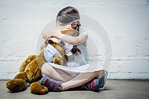 Young girl and her teddy bear wearing protective masks