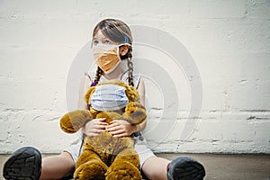 Young girl and her teddy bear wearing protective masks